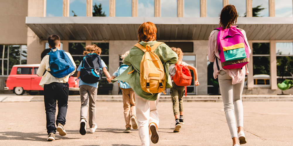 Group of school kids running into the front door of a school