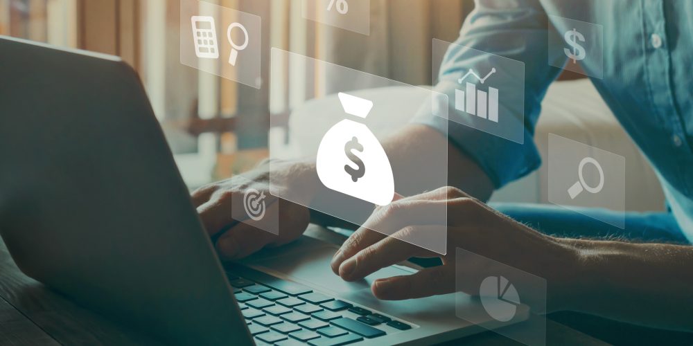 Close up image of a man using a laptop. In the image there are transparent graphics that depict bags of money, calculators, stock charts, and other finance-based images