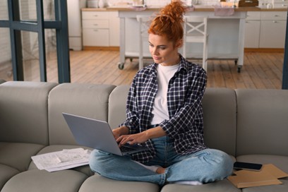 Young entrepreneur working on her laptop from home, managing her business banking online from the couch