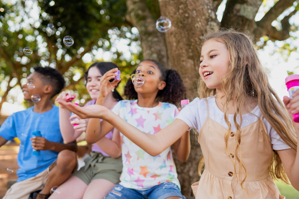Kids sitting outside blowing bubbles together, enjoying a fun and affordable summer activity.