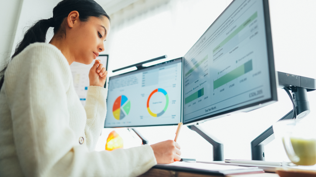 Person reviewing financial data dashboards on multiple monitors using AI-powered banking insights.