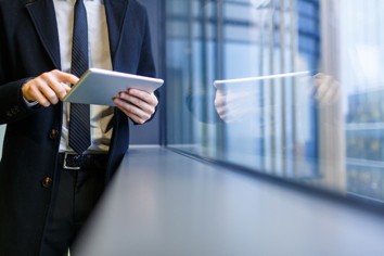 Businessman in suit reviewing banking features on tablet near office window.